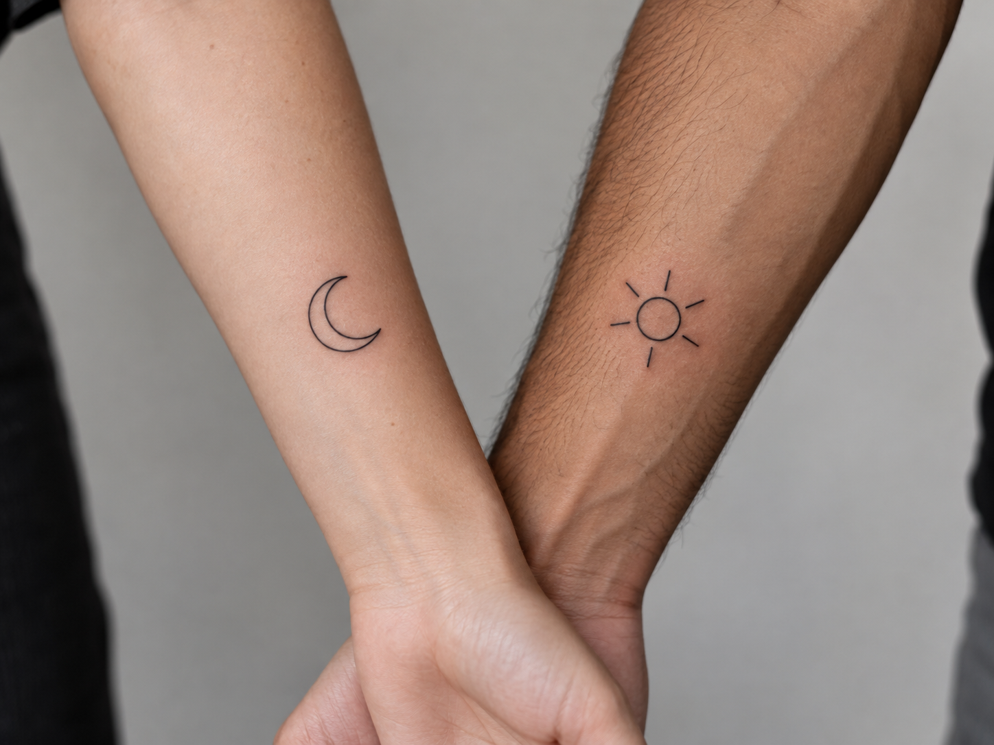 Two forearms with matching black fine-line crescent-moon and sun-burst tattoo symbols
